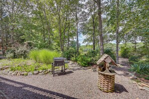 A gravel path with a barbecue grill and a birdhouse in a wooded area.