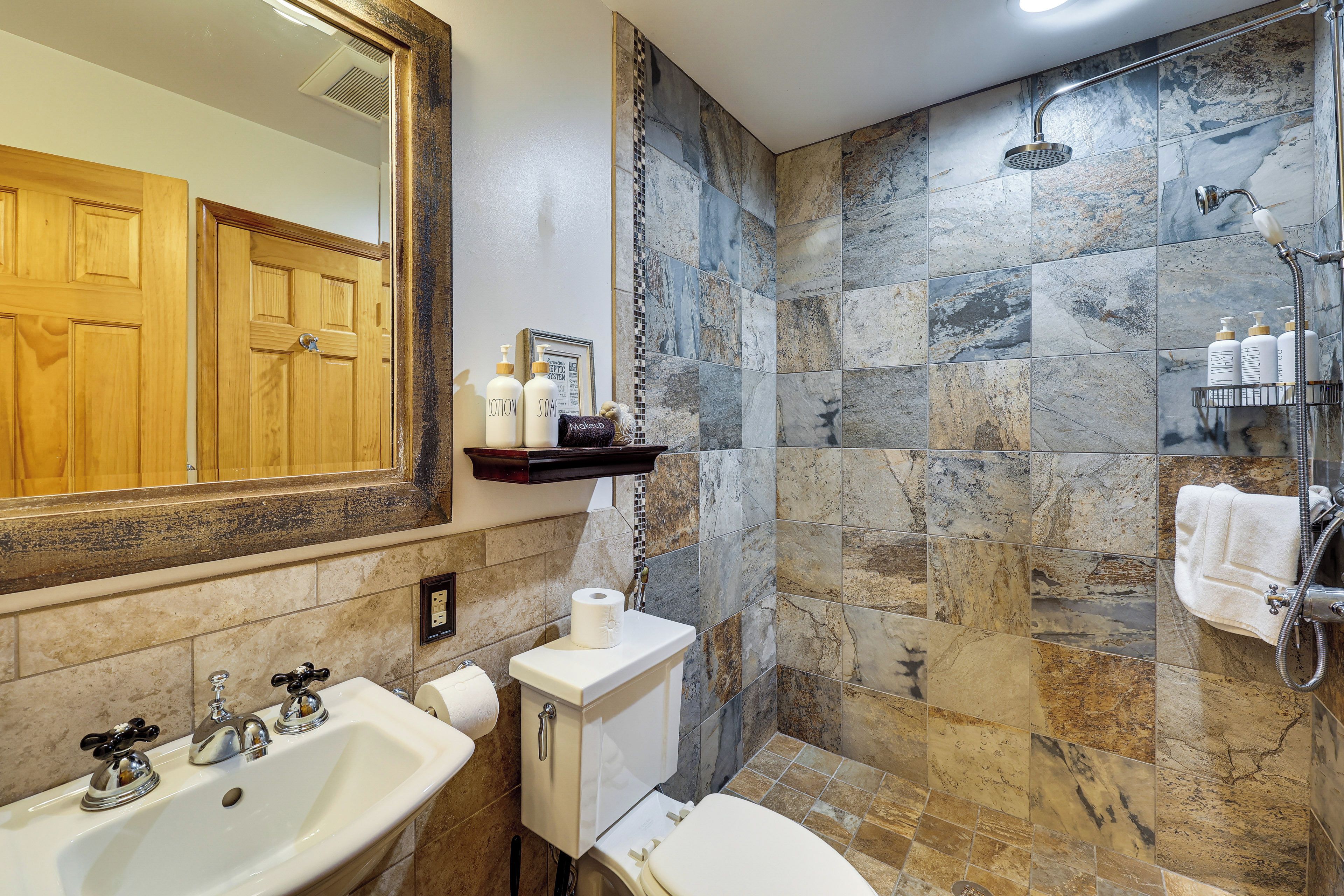 Un bagno con uno specchio grande, un lavandino, un water e una doccia.