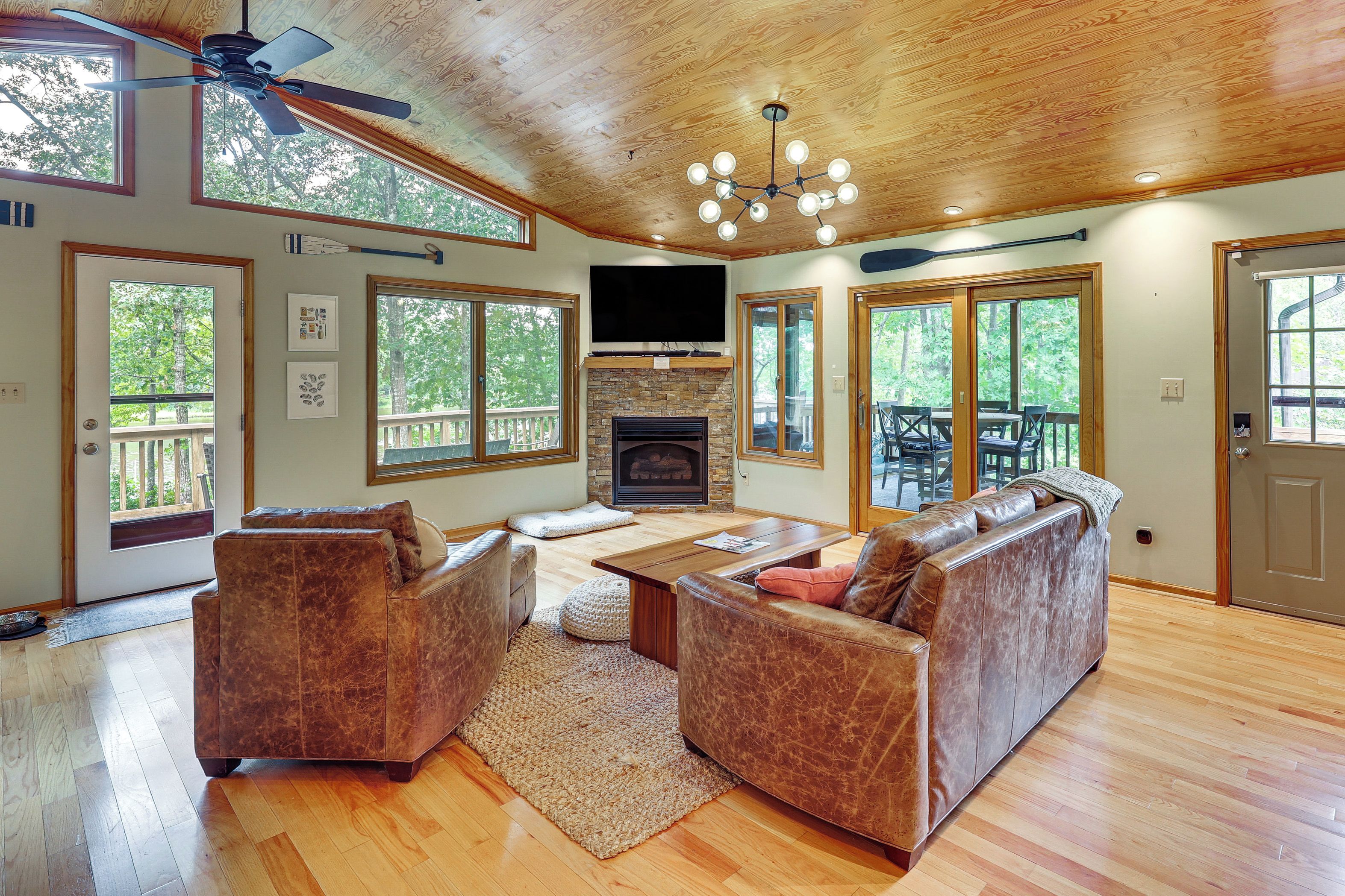 A spacious living room with a fireplace, leather sofas, a coffee table, and large windows offering views of the outdoors.