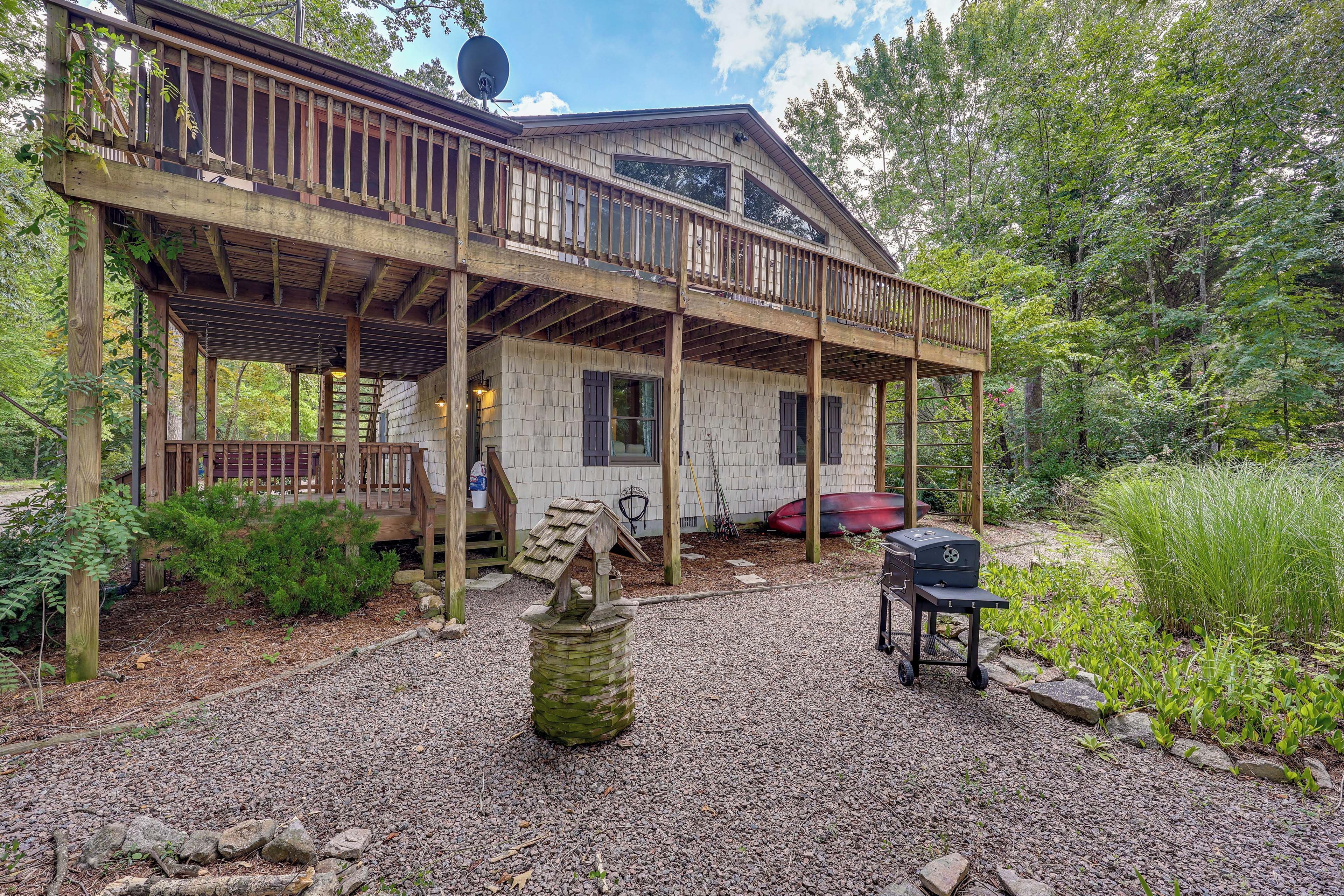 A wooden cabin with a covered porch, a small outdoor grill, and a boat in the background.