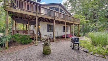 A wooden cabin with a covered porch, a small outdoor grill, and a boat in the background.