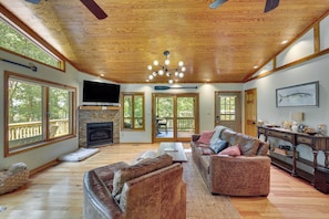 A spacious living room with a fireplace, leather sofas, a television, and large windows.