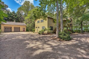 A two-story house with a garage, surrounded by trees and gravel driveway.