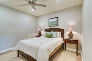 Ein Schlafzimmer mit einem Bett, zwei Nachttischen, einem Deckenventilator, einem gerahmten Bild an der Wand und Teppichboden.