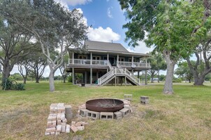 Una casa de dos pisos con porche, un pozo de fuego y un muro de ladrillo.