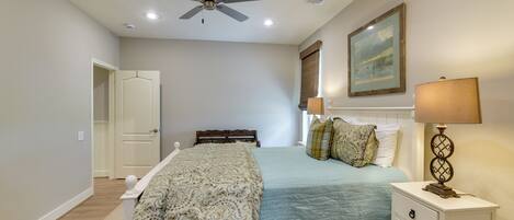 A bedroom with a bed, bedside tables, a ceiling fan, a painting, and a window with blinds.