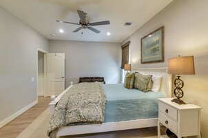 Un dormitorio con cama, mesitas de noche, ventilador de techo, un cuadro y ventana con persianas.