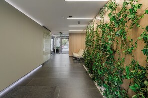 Een hal met een muur bekleed met groene begroeiing, een zithoek met een bank, en een deur naar buiten.