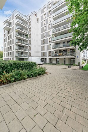 A multi-story residential building with balconies, a paved courtyard, and a white van parked in front. - Lumina Comfort 3-Room Apt with Balcony (Warszawa)