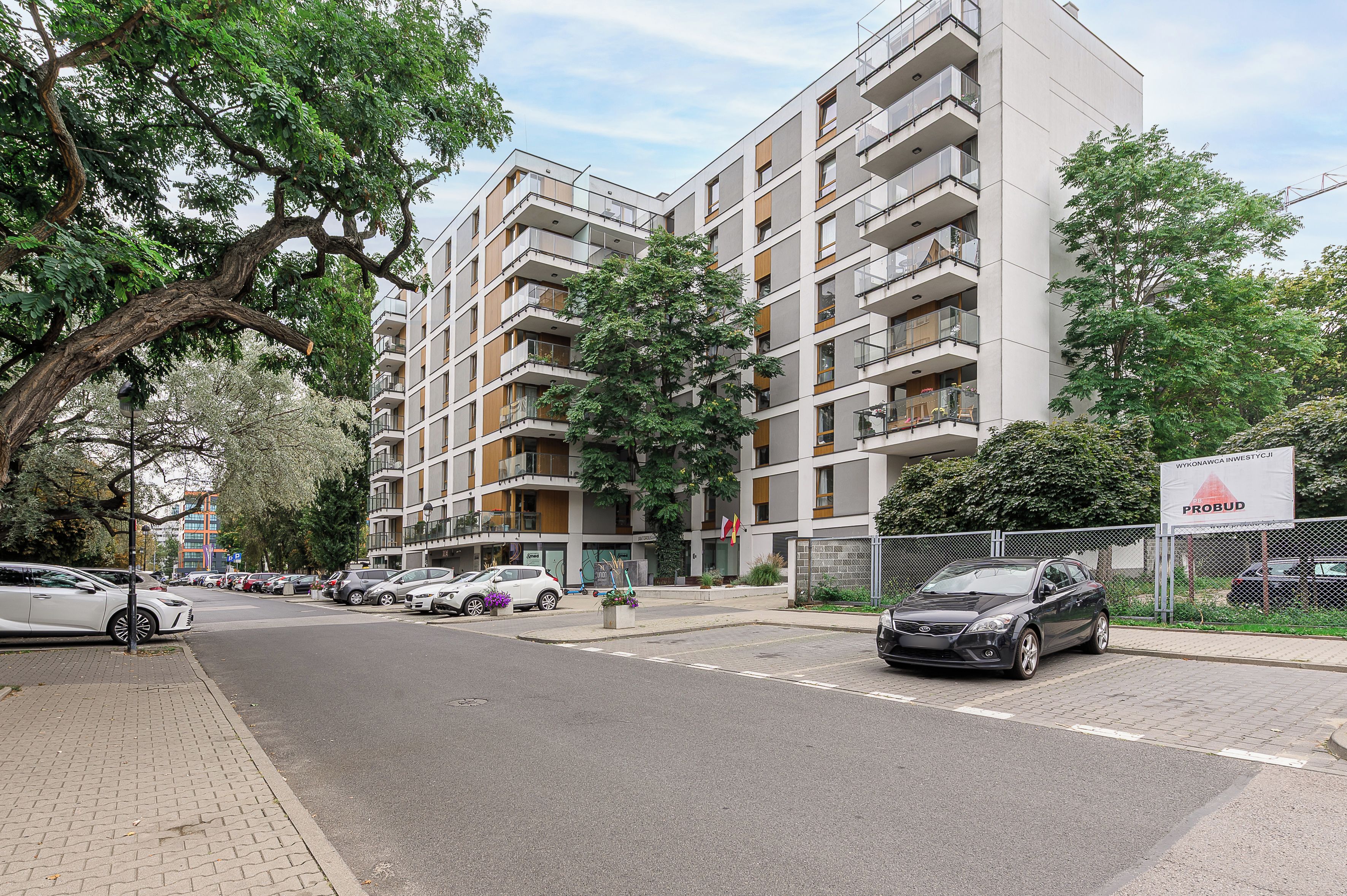 Un edificio residencial de varios pisos con balcones, un área de estacionamiento y una zona de construcción cercada.