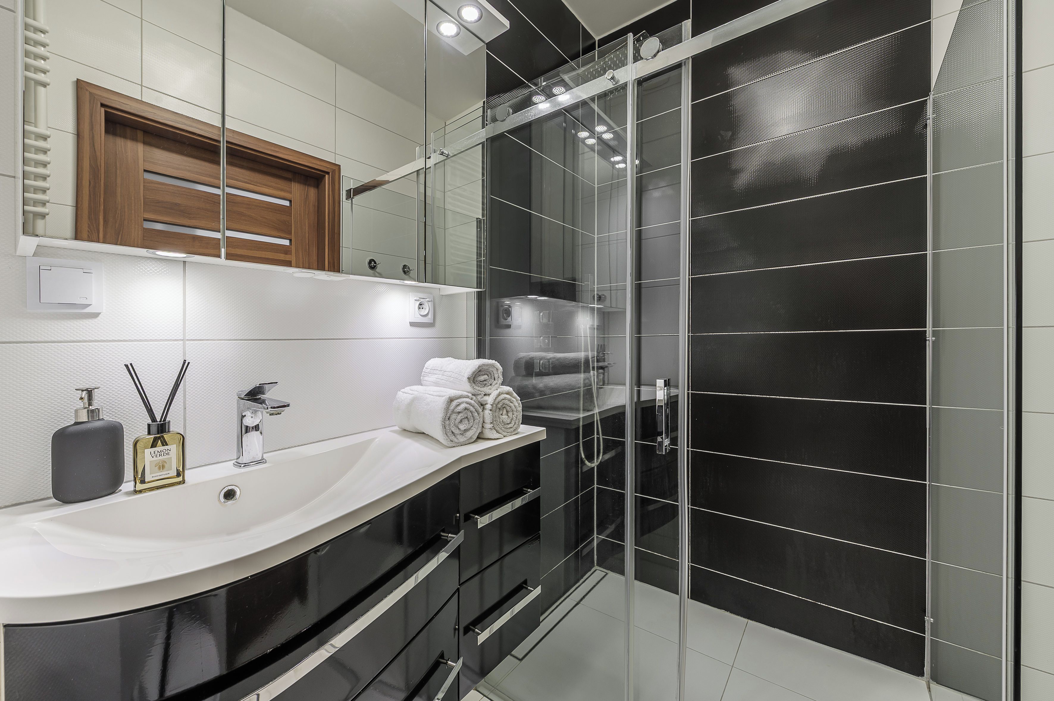 A modern bathroom with a white sink, black cabinet, and a glass shower enclosure.
