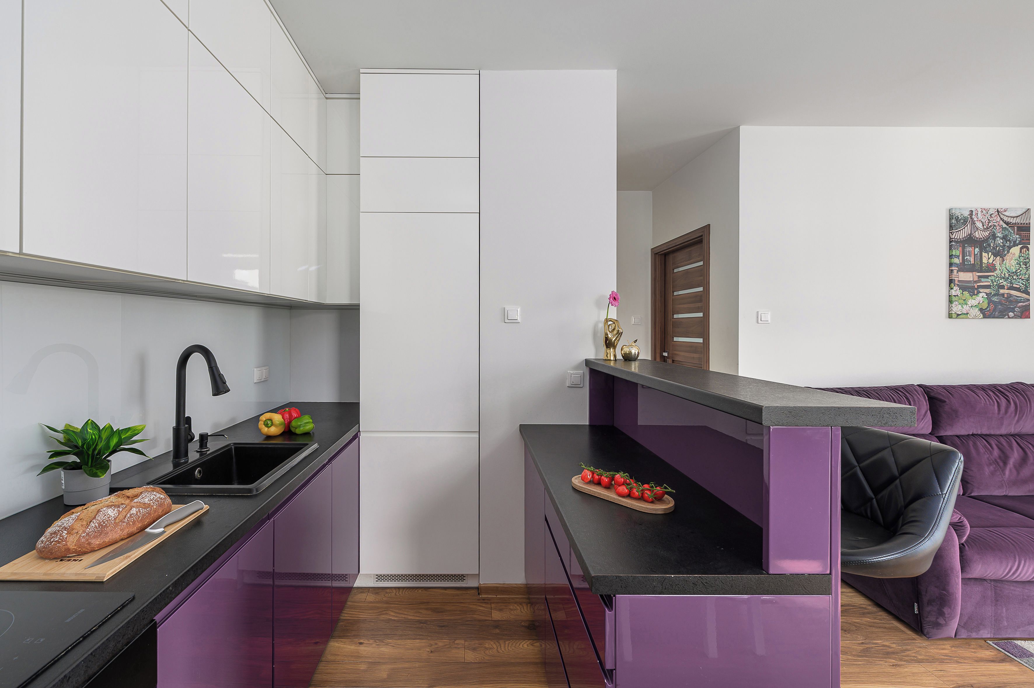 A modern kitchen with a black countertop, white cabinets, and a purple sofa in the living area.