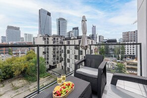 A balcony with wicker furniture, a glass table, and a fruit tray with wine glasses. - Lumina Comfort 3-Room Apt with Balcony (Warszawa)