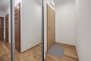 A hallway with wooden doors, a doormat, and a light switch on the wall. - Lumina Comfort 3-Room Apt with Balcony (Warszawa)