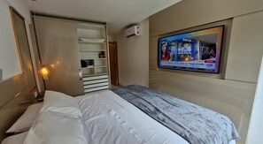 A hotel room with a bed, a TV mounted on the wall, a wardrobe, and a bedside lamp. - Muro Alto - Samoa Polynesia - Porto de Galinhas - Ground floor apartment with private pool. (N. Sra. do Ó)