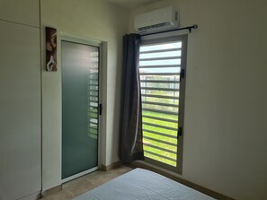 Une pièce dotée d’une porte-fenêtre coulissante donnant sur un balcon, d’un climatiseur blanc fixé au mur et d’un lit avec un matelas blanc.