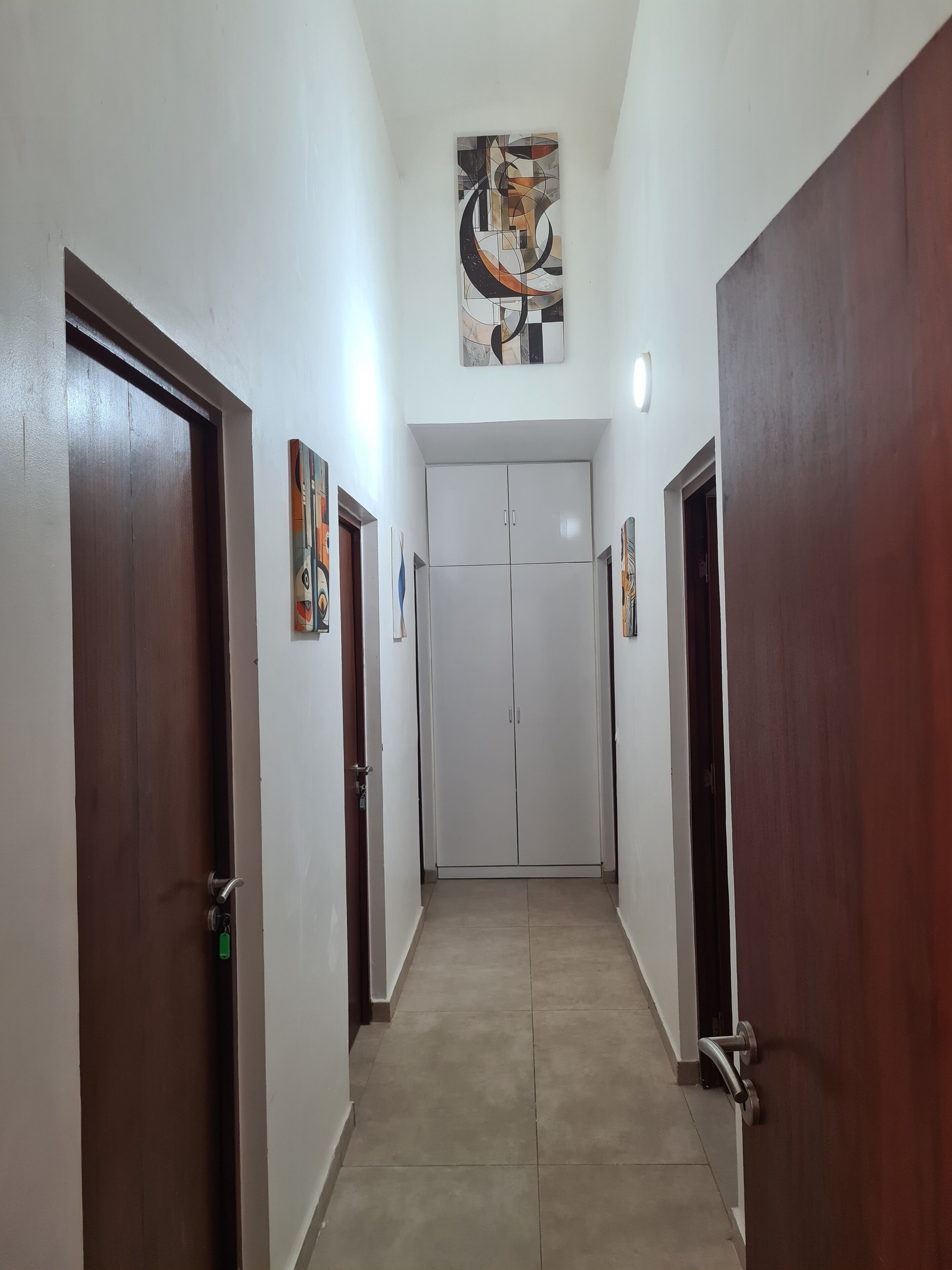 Um corredor com duas portas de cada lado, uma luminária acima e um quadro na parede.