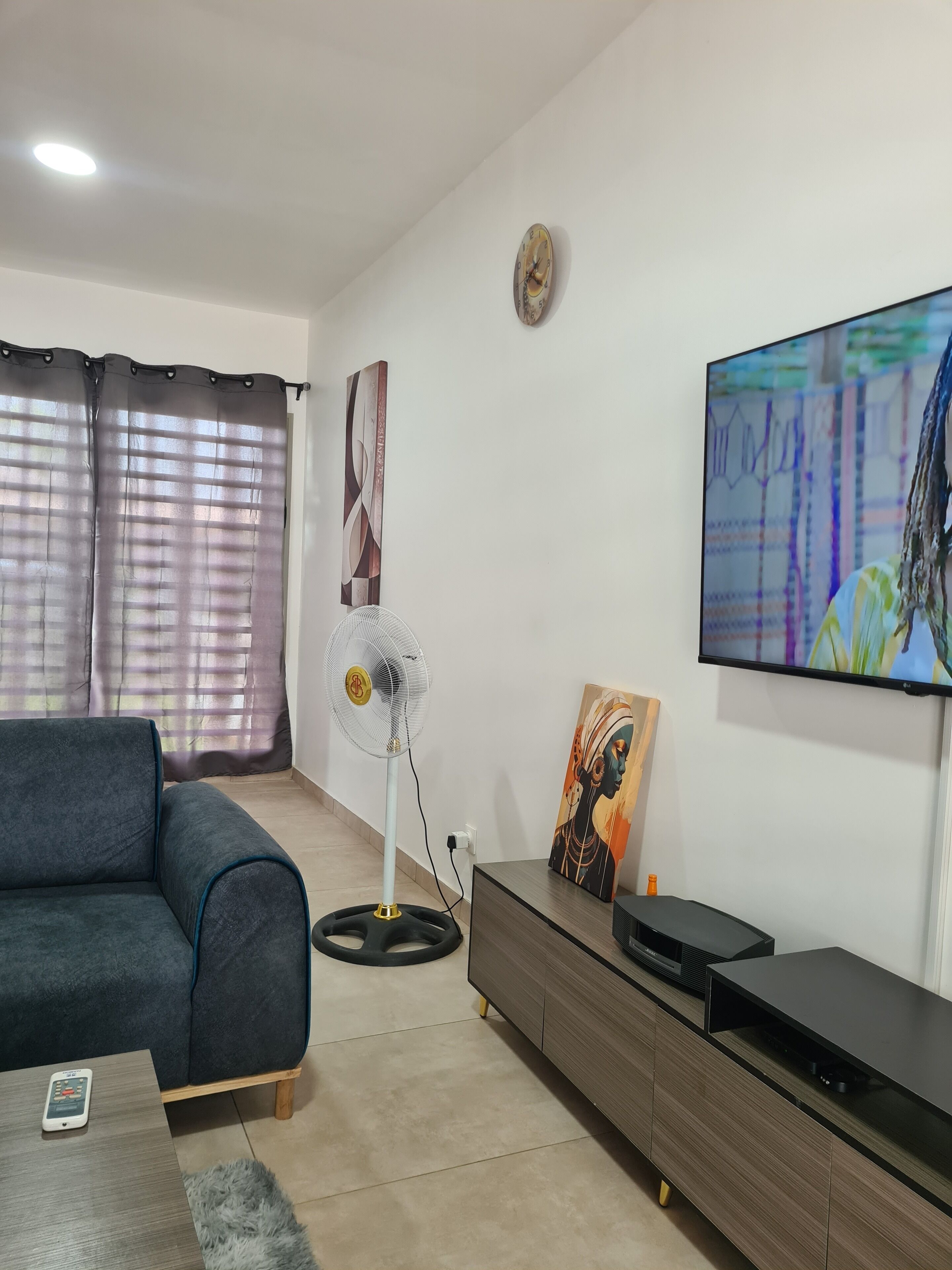 A living room with a sofa, a standing fan, a flat-screen TV, and a painting on the wall.