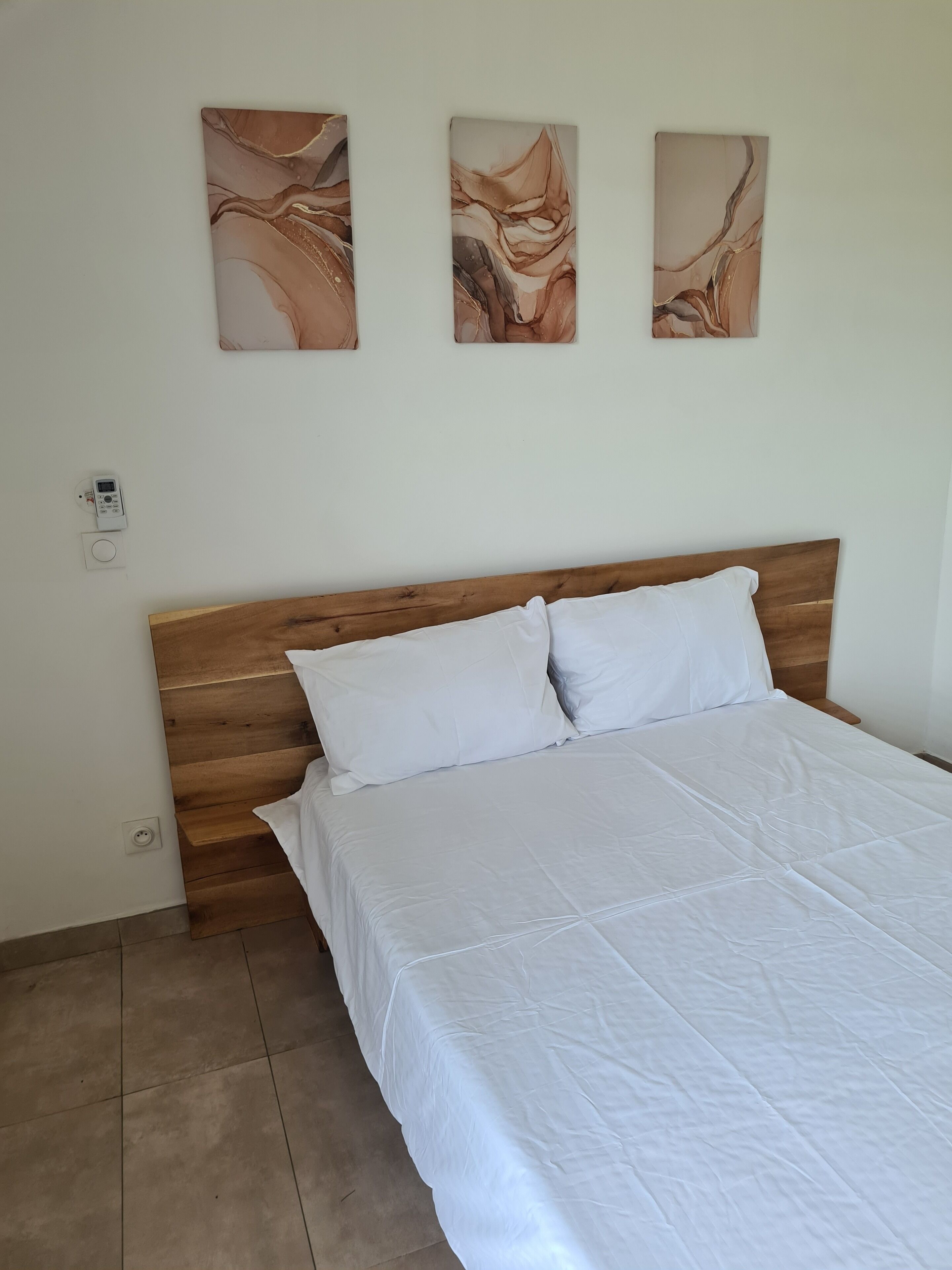 A bedroom with a wooden headboard, a white bedspread, and three abstract paintings on the wall.