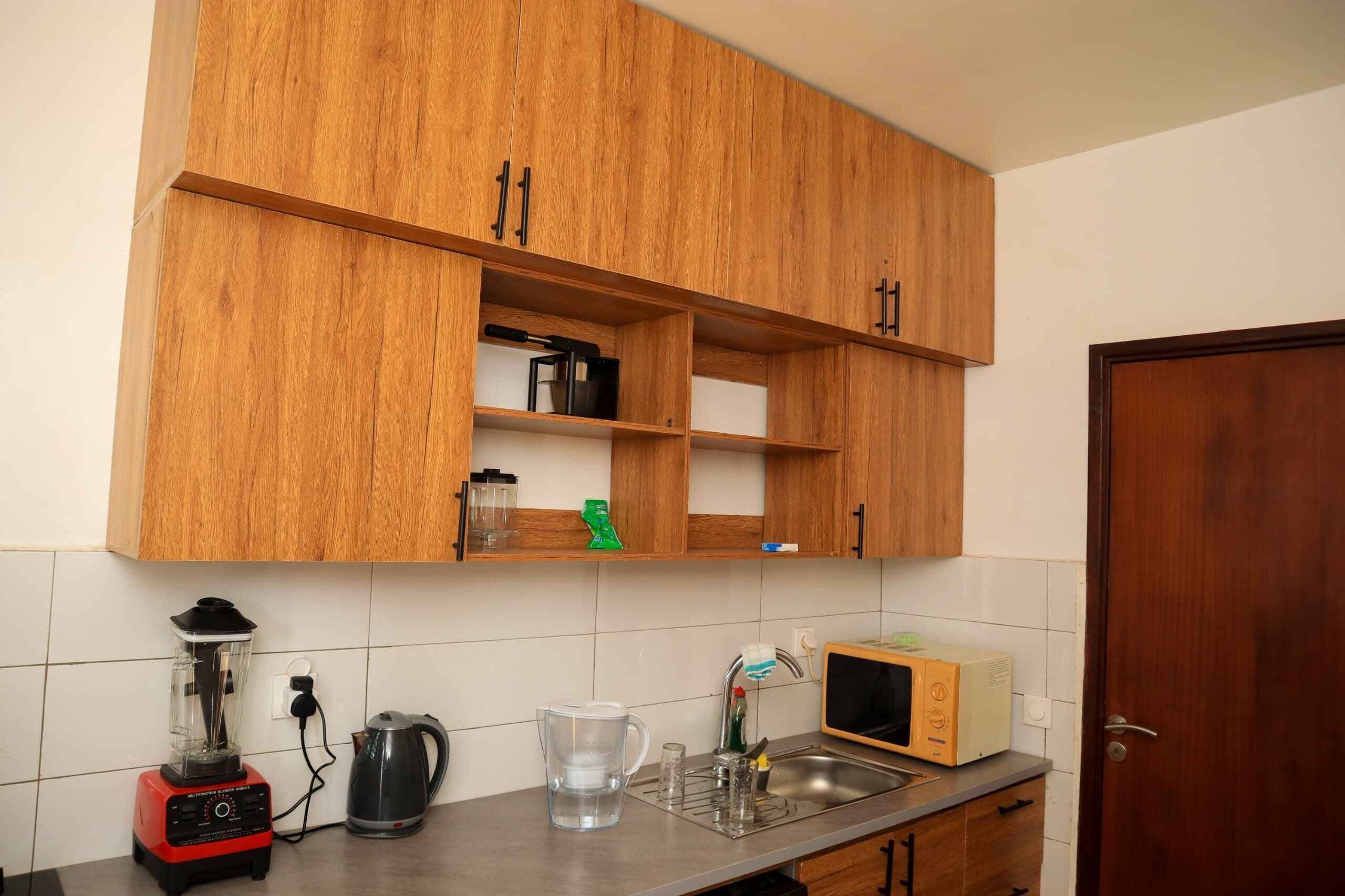 A kitchen with wooden cabinets, a blender, a kettle, a microwave, and a sink.