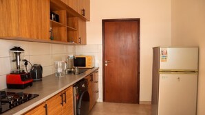 A compact kitchen with wooden cabinets, a microwave, a refrigerator, a washing machine, and a gas stove. - Beautiful villa in Porto-Novo Benin (Porto-novo)