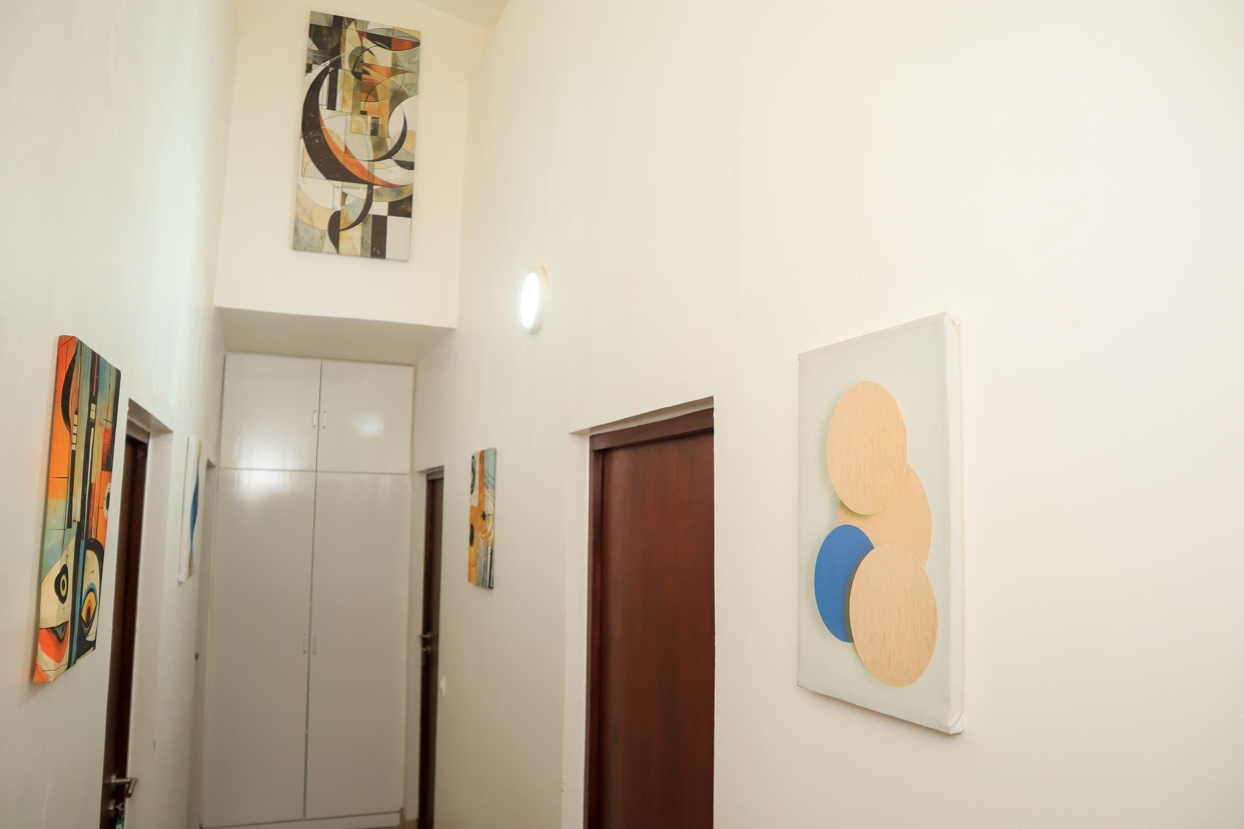 A hallway with a white door, a wooden door, and two pieces of wall art.