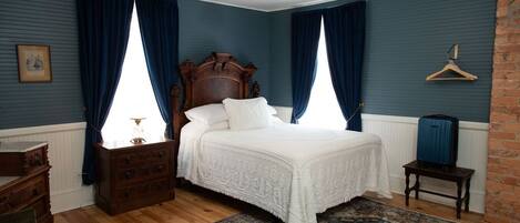 A bedroom with a large bed, wooden dresser, and a hanging coat rack.