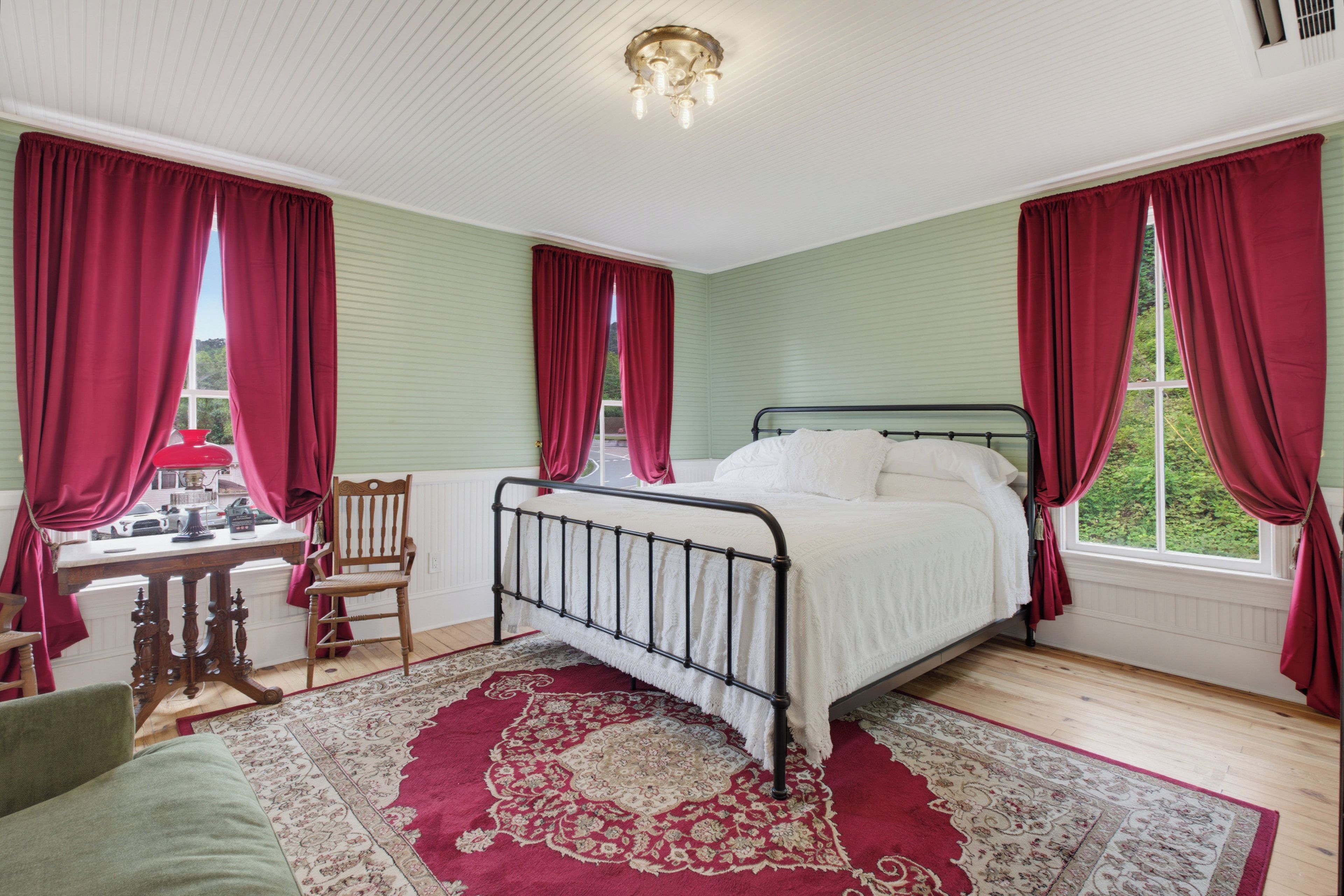 Un dormitorio con cama, una silla, una mesa y un ventanal con cortinas.