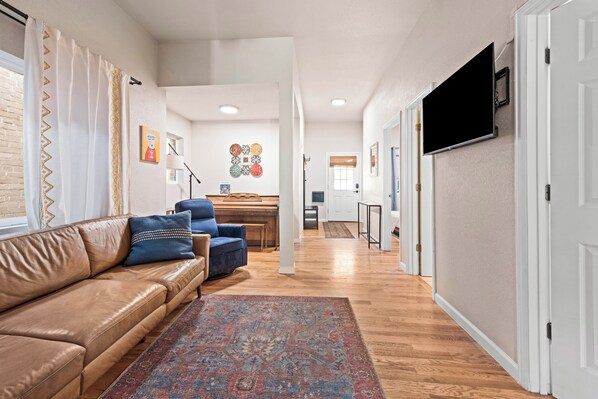 A modern living room with a leather sofa, a patterned rug, and a flat-screen TV mounted on the wall.