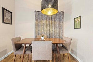 A dining area with a wooden table, four chairs, a vase with flowers, and a wall-mounted lamp.
