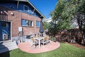 Une terrasse à l’arrière de la maison, avec une table et des chaises, un barbecue et une maison en briques.
