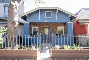 A two-story house with a blue facade, a brick chimney, and a front gate.