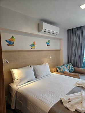 A hotel room with a bed, a sofa, a wall-mounted air conditioner, and decorative sailboat wall art. - F4.009 | Practicality, charm and comfort/Carneiros (Tamandaré)