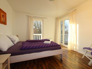 A bedroom with a bed, a chair, a window, and a balcony. - Holiday Apartment W17.2 (Graal Mueritz)