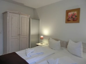 Quarto de hotel com cama, guarda-roupa, mesa de cabeceira com abajur e um quadro na parede.