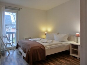 Quarto com cama, mesa de cabeceira, abajur e uma cadeira.