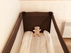 Ein Bett mit weißer Matratze und dunklem Kopfteil, ein Teddybär auf der Matratze und eine weiße Wand mit Ziegelmuster.