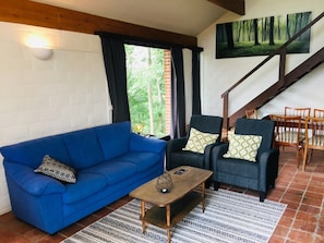 Ein Wohnzimmer mit einem blauen Sofa, zwei Sesseln, einem Couchtisch und einer Treppe.