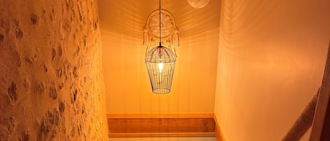 Una escalera con barandilla de madera y cuerda, que lleva a un rellano con un aplique de pared y un cuadro enmarcado.