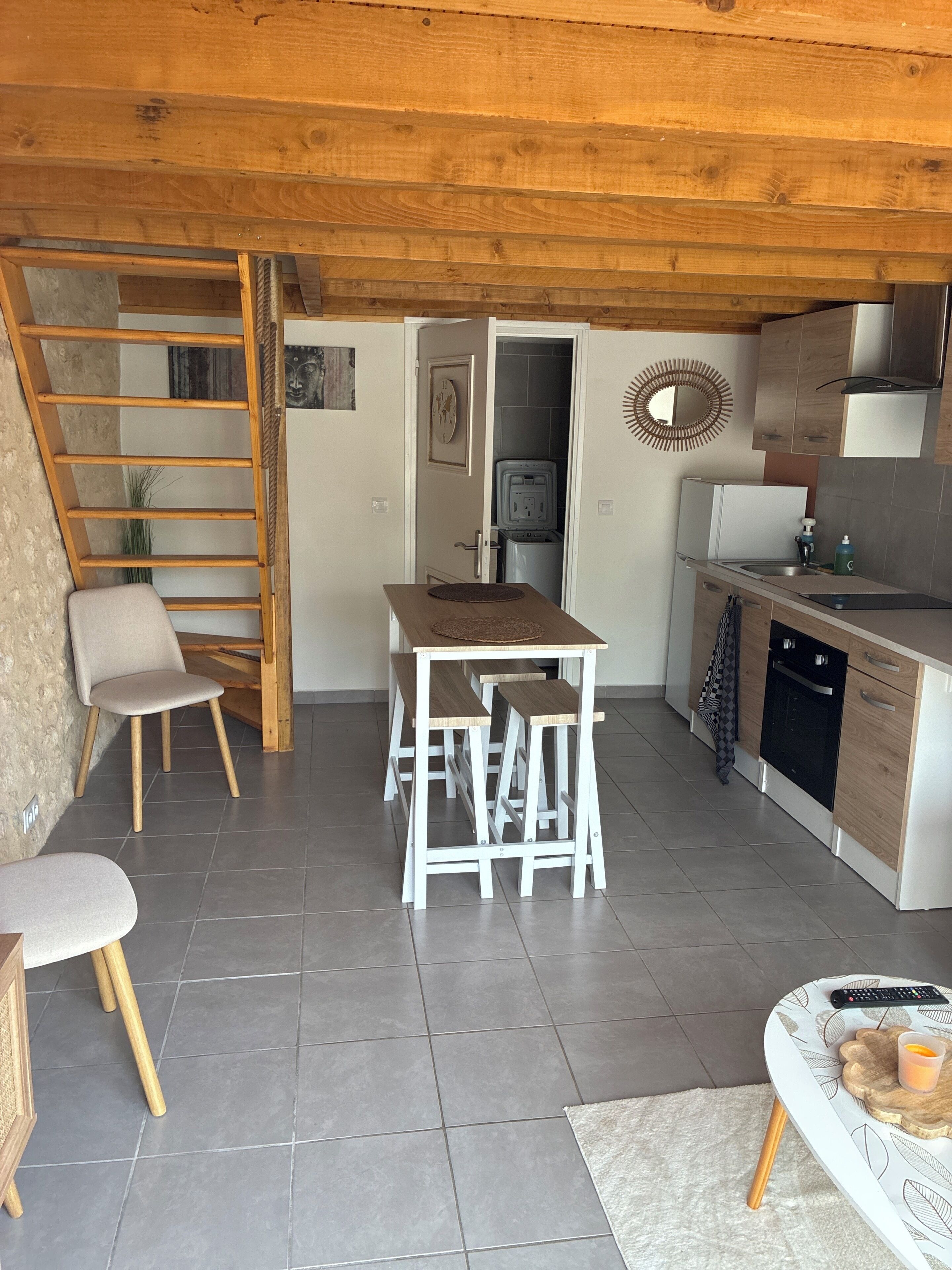 Eine kleine Küche mit Holztisch, Hockern und einem eingebauten Backofen.