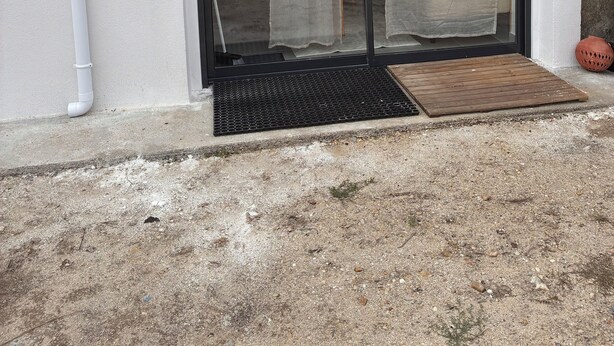 A building with a white exterior, a black sliding glass door, a white pipe, and a small brown door mat.