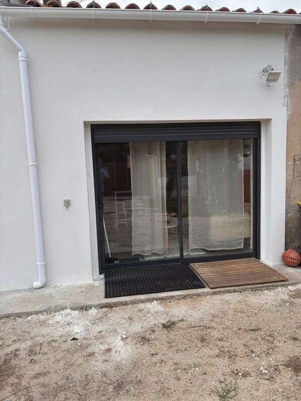 Un edificio con fachada blanca, una puerta corredera de vidrio negro, una tubería blanca y un felpudo marrón pequeño.