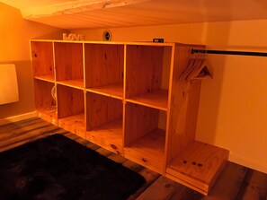 Una estantería de madera con varios compartimentos, una radio pequeña y un perchero con objetos colgados.