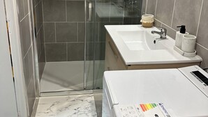Moderni kylpyhuone, jossa on lasiseinällinen suihku, valkoinen pesuallas marmoritasolla ja peili pesualtaan yläpuolella.