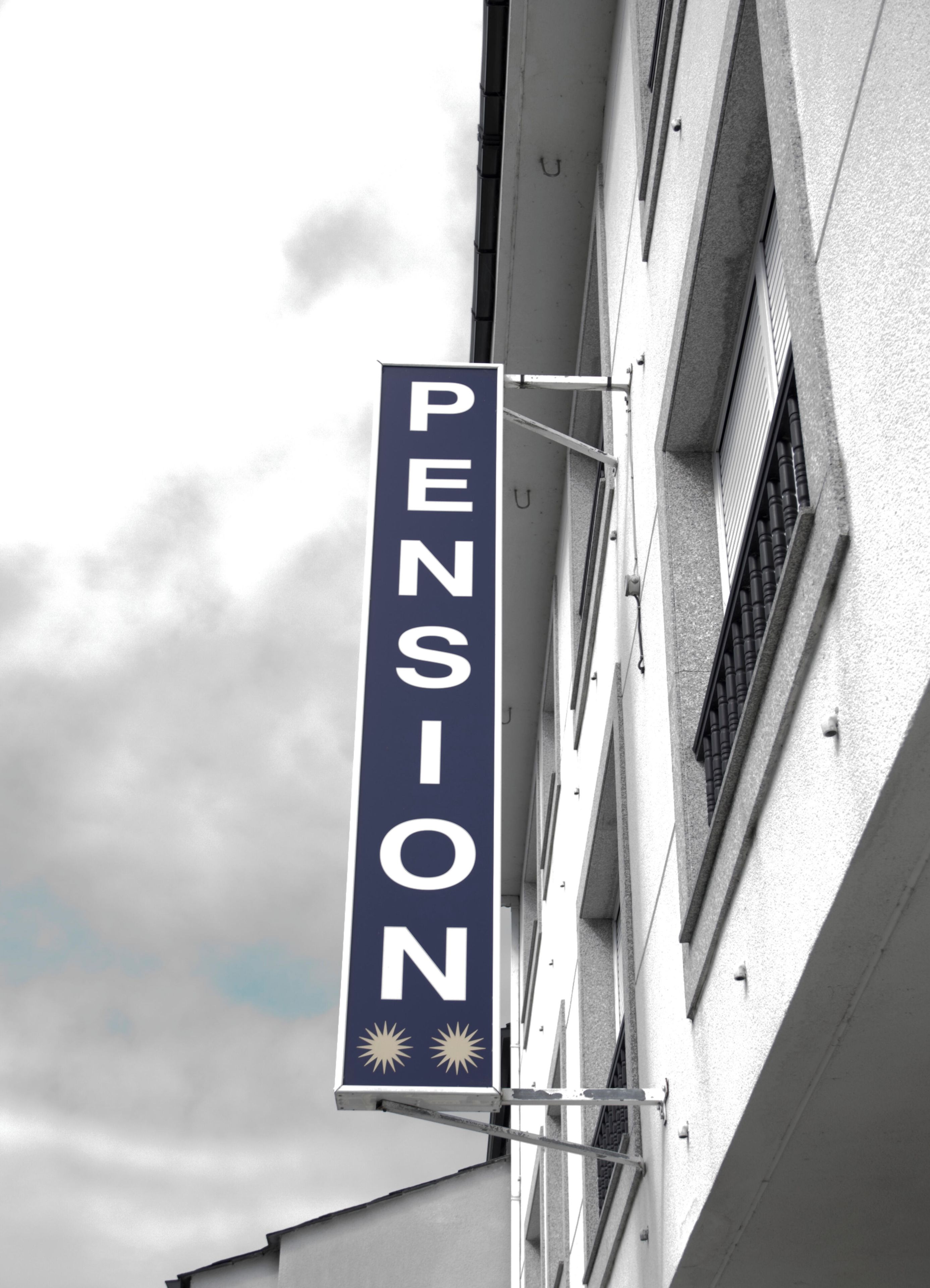 Et vertikalt skilt med ordet 'PENSION' og to sol-symboler, monteret på en bygning.