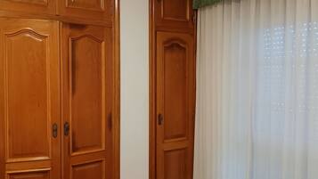 Una habitación con armarios de madera, una cama con cubrecama a rayas y un ventanal con cortinas traslúcidas.