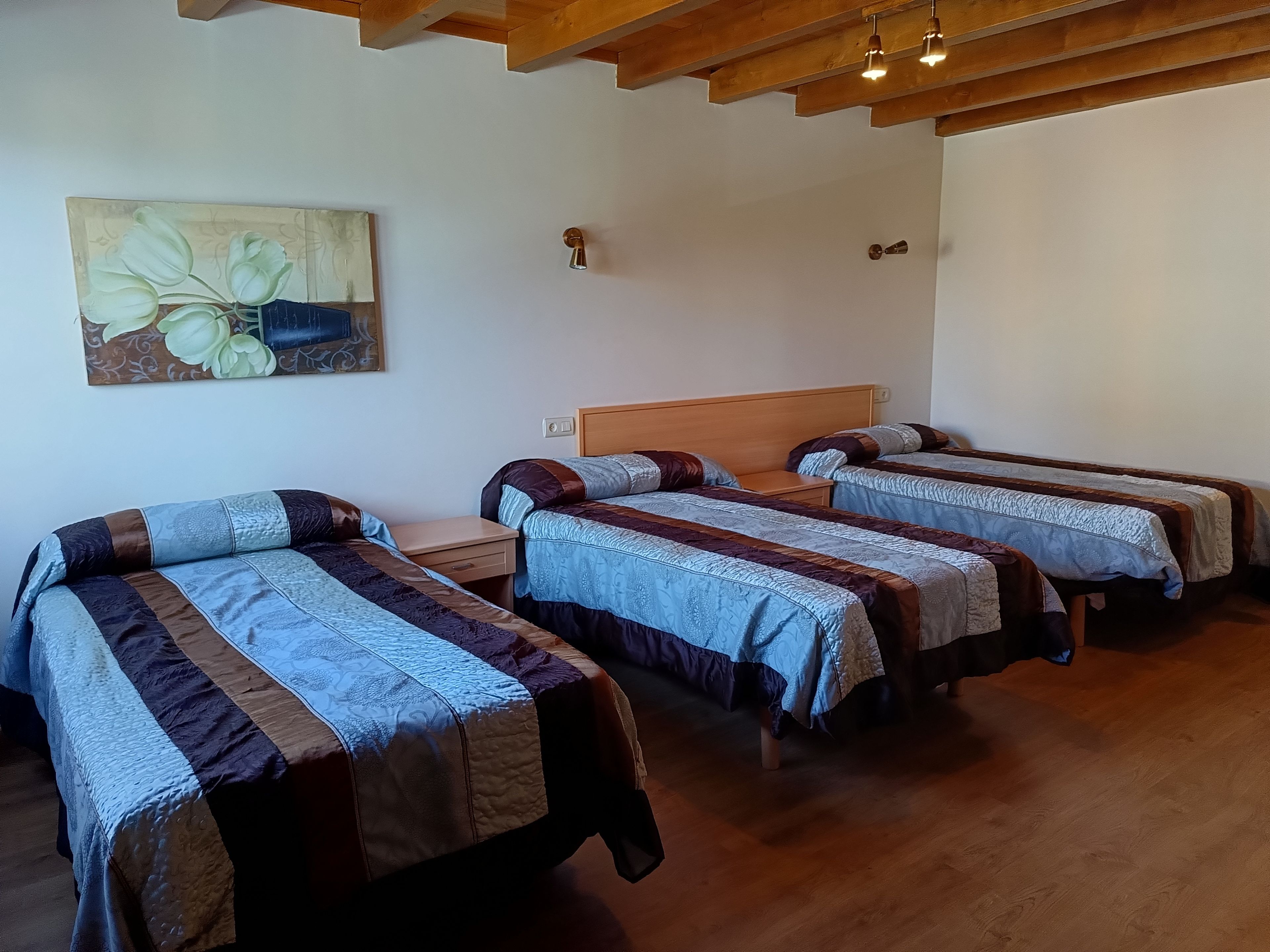 Une chambre avec trois lits, un plancher en bois et un tableau au mur.