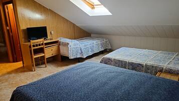 A dormitory room with a sloped ceiling, a skylight, a desk with a computer, two beds with patterned bedding, and a wooden wardrobe.