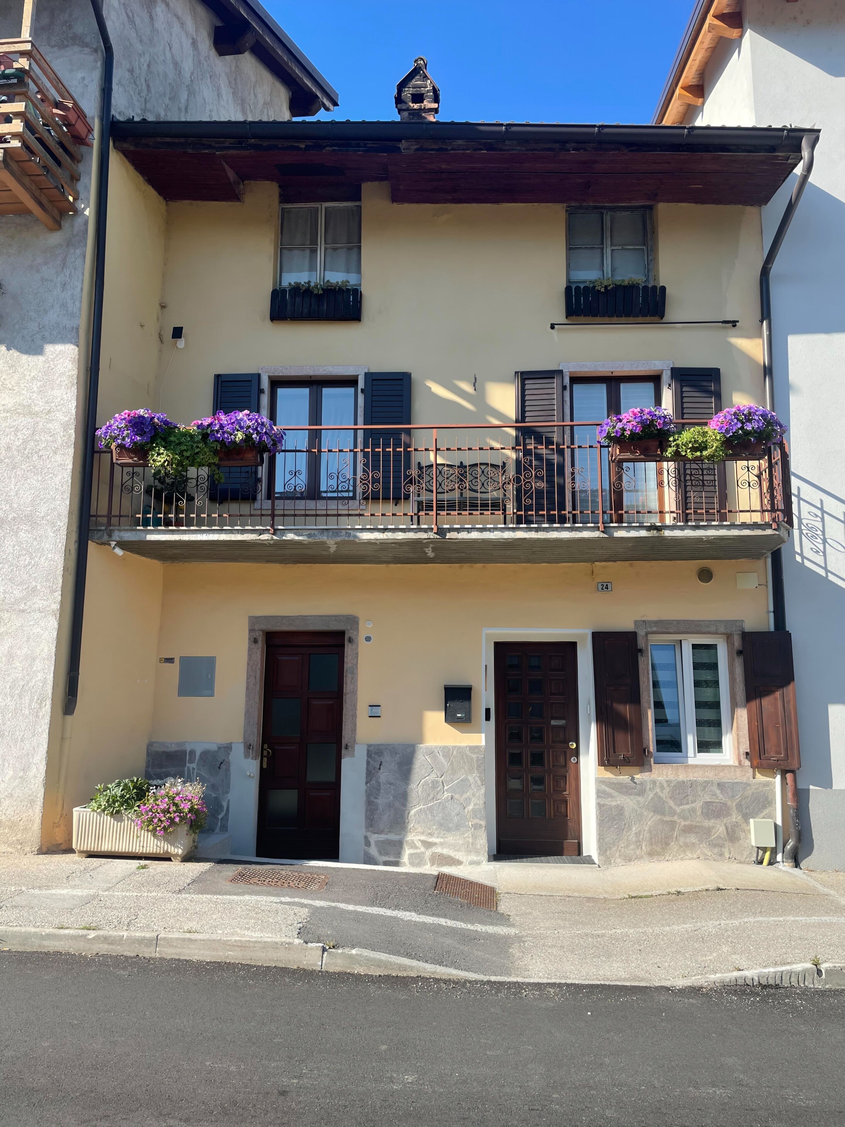 Un immeuble de deux étages doté d’un balcon, de volets en bois et de jardinières.