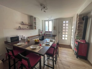 Een keuken met een centraal eiland, een magnetron en een fornuis. Er staan stoelen en een tafel gedekt voor een maaltijd.